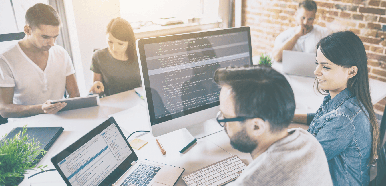 Development team collaborating around code on multiple screens